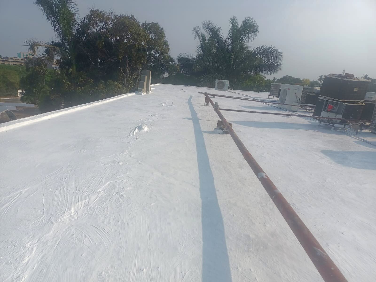 Perspectiva larga de azotea terminada con membrana gris instalada, pretil y ciudad al fondo